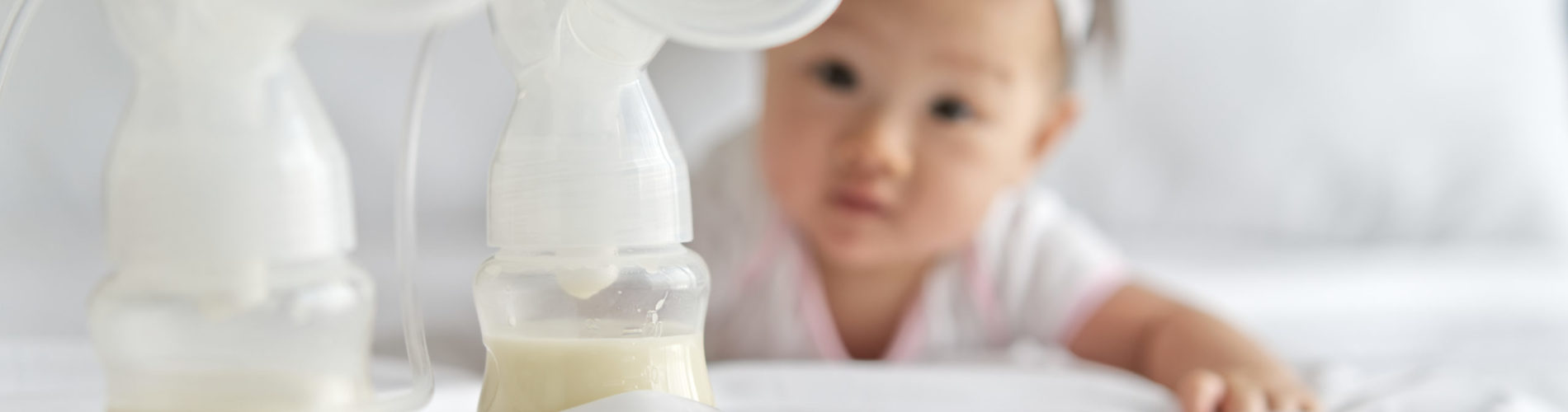 Breast milk in milk pump's bottles on the bed with little cute baby crawling in background